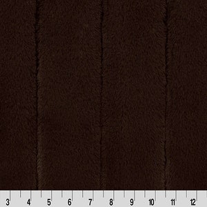 May include: A close-up of a dark brown plush fabric with a vertical ribbed texture. The fabric is soft and fuzzy, and it appears to be a luxurious material.