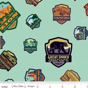 May include: A light teal fabric featuring various national park patches. Patches include "Zion," "Great Smoky Mountains," "Petrified Forest," and "Capitol Reef." The patches are in shades of brown, green, and blue.
