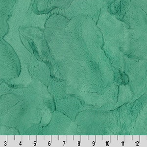 Puede incluir: Primer plano de una tela de piel sintética de color verde azulado. La tela tiene una textura suave y afelpada y un sutil patrón de mármol.