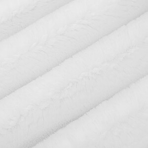 May include: White faux fur fabric with a soft, fluffy texture. The fabric is arranged in diagonal lines, creating a subtle pattern.
