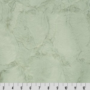 May include: A close-up of a soft, plush fabric in a light sage green colour. The fabric has a fuzzy, textured surface that resembles fur.