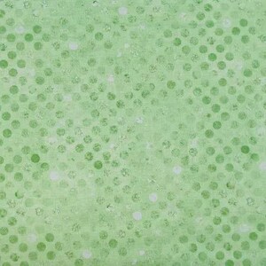 May include: A light green fabric featuring a repeating pattern of darker green circular dots. The surface has a textured, slightly distressed appearance with subtle variations in color intensity across the dotted design elements.
