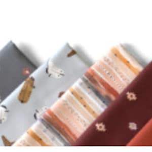 Pu&ograve; includere: L'immagine mostra campioni di tessuto piegati in fila, con il testo "WILD WEST" e "BY BOCCACCINI MEADOWS" sopra. I tessuti presentano vari motivi, tra cui disegni floreali e geometrici, in colori come nero, grigio e ruggine.