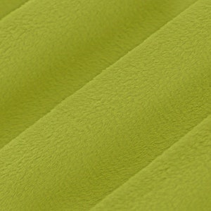 May include: Close-up of a soft, lime green fabric with a plush texture. The fabric is arranged in diagonal, parallel lines, creating a textured surface. The material appears to be a cosy, possibly a blanket or upholstery.