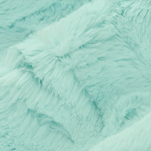 May include: Close-up of a soft, light blue faux fur fabric. The fabric has a fluffy texture and a subtle sheen.