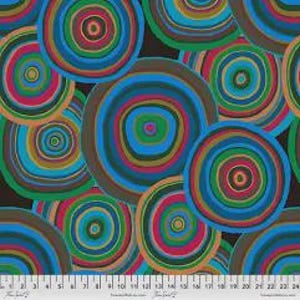 May include: A fabric featuring a repeating pattern of colourful concentric circles in shades of blue, green, red, and brown. The circles vary in size and overlap, creating a vibrant design. A ruler with inch measurements is at the bottom.