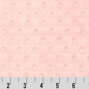 May include: A close-up of a pale pink fabric with a textured, raised dot pattern. The fabric is measured in inches.
