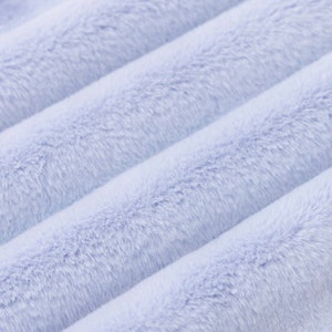 May include: Close-up of a soft, light blue fabric with a fuzzy texture. The fabric is folded in a way that creates a series of parallel lines.