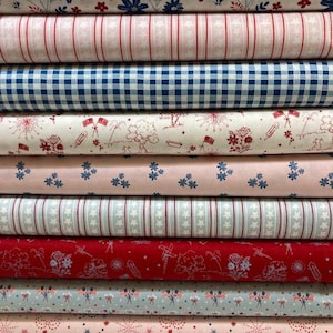May include: A stack of ten folded fabric bolts featuring various patterns including blue and red floral prints, pink and white stripes, blue gingham checks, patriotic motifs with flags and fireworks, and star patterns in red, white, and blue.