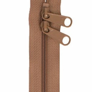 Puede incluir: Una cremallera marrón con dos tiradores, uno encima del otro. Los dientes de la cremallera son de un marrón más oscuro que la cinta de tela. Los tiradores tienen una abertura circular. La cremallera está sobre un fondo blanco.