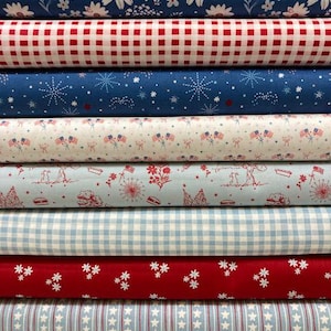 May include: A stack of ten fabric bolts featuring various patterns including white floral prints on blue, red and white gingham, blue with white starbursts, American flag motifs, light blue with red illustrations, and blue with white stars.