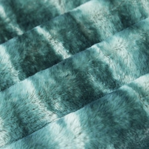 May include: Close-up of a teal blue faux fur fabric with a tie-dye pattern. The fabric has a soft, plush texture.