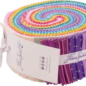 Puede incluir: Un rollo de tiras de tela coloridas en espiral. La tela presenta un arcoíris de colores, incluyendo rosa, amarillo, azul y morado. Una cinta blanca con el texto "Free Spirit" envuelve la tela. Ideal para acolchado y manualidades.