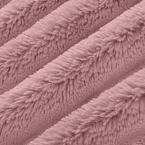 May include: Close-up of a soft, plush fabric with a pink hue. The fabric has a fuzzy, textured surface with a subtle striped pattern.