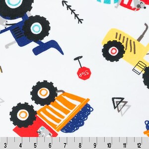 May include: White fabric featuring a repeating pattern of colorful construction vehicles including blue, yellow, and orange tractors and dump trucks driven by animals, red stop signs, and black geometric shapes, with a 15-inch ruler at the bottom.