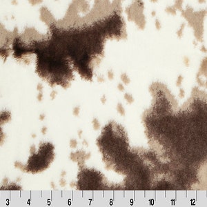 May include: White faux fur fabric with brown and beige spots. The fabric has a soft, fuzzy texture.