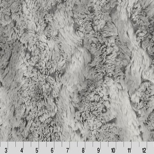 Pode incluir: Um close-up de um tecido de pele sintética macio, cinza, com um padrão sutil de redemoinhos. O tecido tem uma textura felpuda e um visual luxuoso.