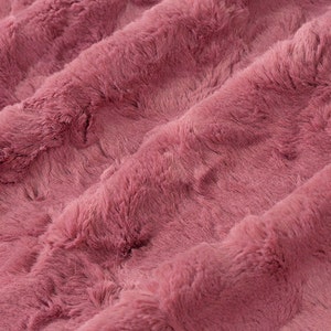 Peut inclure: Gros plan sur un tissu doux et pelucheux de couleur rose poudré. Le tissu a une texture duveteuse et un motif rayé subtil.