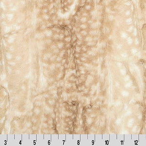May include: A close-up of a beige faux fur fabric with a white spotted pattern. The fabric has a soft, plush texture.