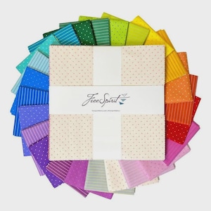 Puede incluir: Un conjunto de cuadrados de tela coloridos dispuestos en un patrón circular. Los cuadrados presentan varios diseños, incluyendo lunares y rayas, en tonos de azul, verde, amarillo, naranja y rosa. El centro presenta una etiqueta blanca con el texto "Free Spirit".