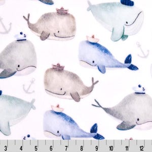 Könnte beinhalten: Ein weißer Stoff mit einem sich wiederholenden Muster aus Aquarell-Walen, die Matrosenhüte tragen. Die Wale sind in Blautönen, Grau und Braun gehalten.