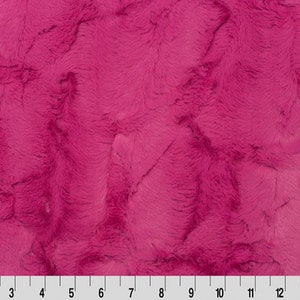 May include: A close-up of a soft, pink faux fur fabric. The fabric has a fluffy, textured surface.