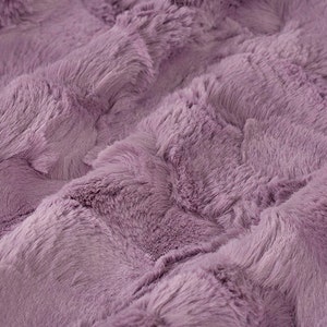 May include: A soft, plush fabric in a light purple colour. The fabric has a textured, fluffy appearance.