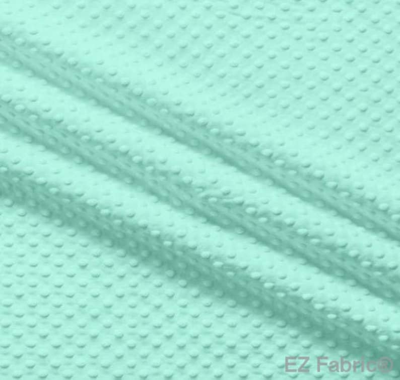 Op de afbeelding: Close-up van een mintgroene stof met een getextureerd, gestippeld patroon. De stof is gevouwen, waardoor diagonale lijnen over de afbeelding ontstaan. Het materiaal lijkt zacht en pluche, geschikt voor diverse knutselprojecten.