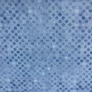 May include: A light blue fabric featuring a repeating pattern of darker blue polka dots. The surface has a subtle, mottled texture with small, shimmering silver-toned flecks distributed throughout the design, creating a speckled appearance.