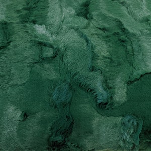 May include: A close-up of a soft, plush fabric in a deep green color. The fabric has a fuzzy texture and a slightly mottled appearance.