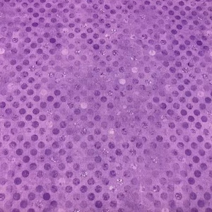 May include: A purple fabric featuring a repeating pattern of darker purple polka dots. The surface has a subtle, shimmering, glittery texture integrated into the design, creating a light-reflecting effect across the entire textile surface.