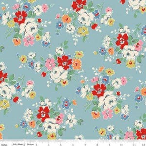 May include: A light blue fabric featuring a repeating floral pattern of white, red, pink, orange, and yellow flowers with green leaves. A white ruler is visible at the bottom edge, showing measurements in inches from 0 to 12 inches.