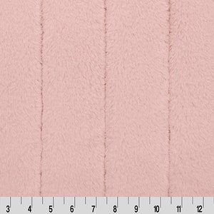 May include: A close-up of a soft, pink, fuzzy fabric with a subtle vertical texture. The fabric is measured in inches.
