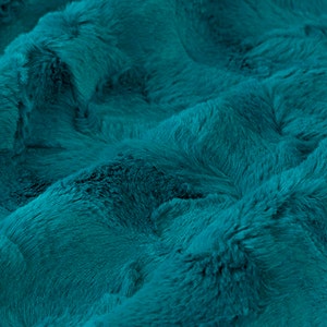 May include: Close-up of a teal blue faux fur fabric. The fabric has a soft, plush texture.