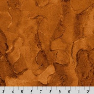 May include: A close-up of a brown faux fur fabric with a swirling pattern. The fabric has a soft, plush texture.