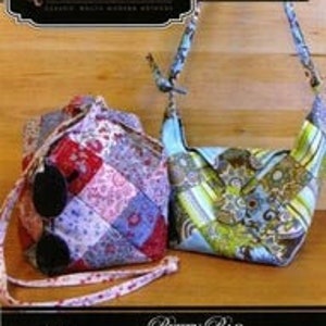 May include: Two fabric handbags, one red, white, and blue patchwork, the other blue and green floral. The bags have straps and are displayed on a wooden surface. The text "Quiltsmart" and "Betty Bag" are visible.