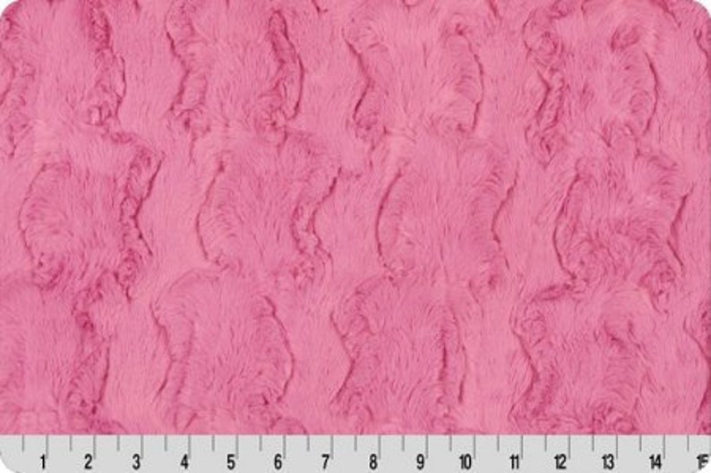 May include: Pink faux fur fabric with a textured, wavy pattern. The fabric has a soft, plush feel.