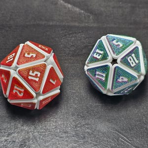 May include: Two twenty-sided dice with white frames and textured, shimmering faces. The left die features orange and red gradient faces with white numbers, while the right die displays iridescent green and blue gradient faces with white numbers.