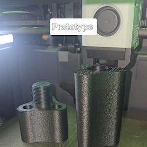 May include: Two black 3D-printed prototype parts. One part has a threaded top and two side holes. The other part is a tall, cylindrical shape. The word "Prototype" is displayed in a white rectangle.