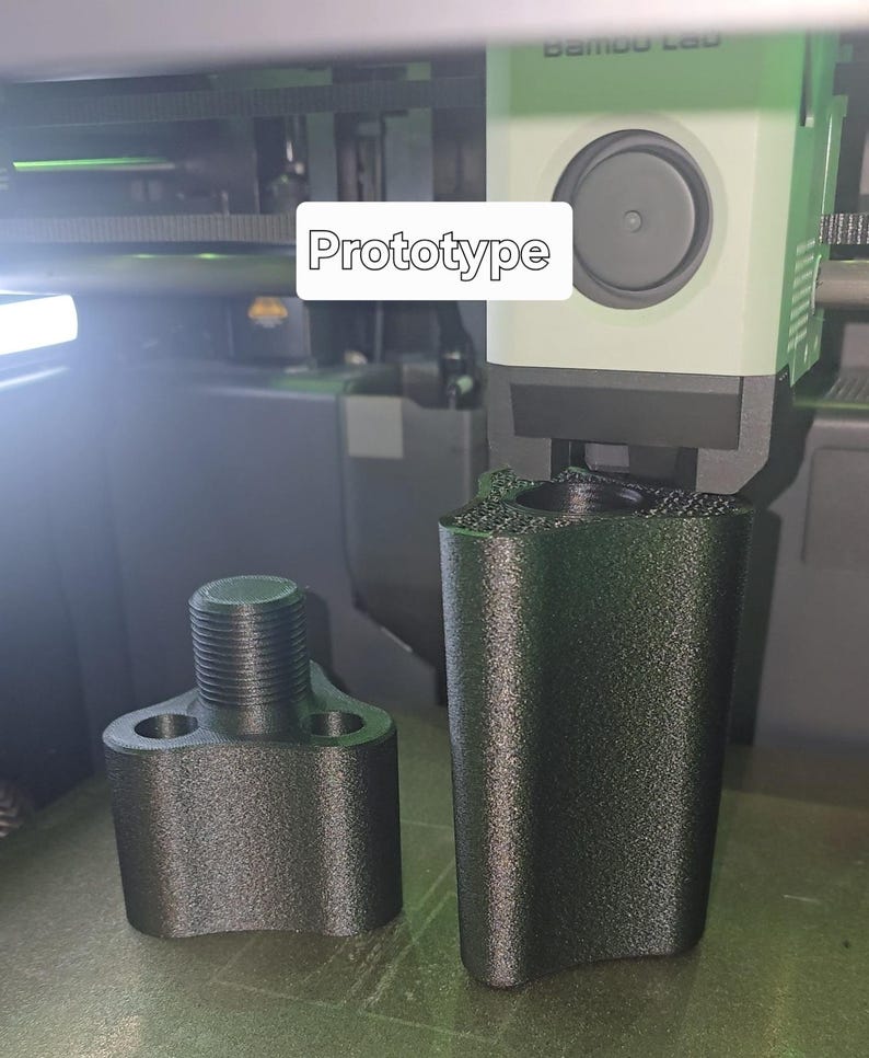 May include: Two black 3D-printed prototype parts. One part has a threaded top and two side holes. The other part is a tall, cylindrical shape. The word "Prototype" is displayed in a white rectangle.