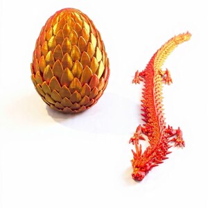 May include: A golden-orange, textured dragon egg and a red and orange dragon figurine. The egg is oval-shaped and made of overlapping, scale-like segments. The dragon is detailed with a spiky spine and outstretched limbs, and is lying down.