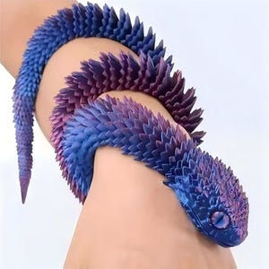 May include: A flexible, articulated snake toy featuring a gradient colour scheme that transitions from deep blue to vibrant purple. The surface is covered in numerous small, pointed, scale-like protrusions, and the head displays a prominent eye.