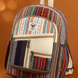 Puede incluir: Mochila colorida con una variedad de patrones tejidos en rojo, azul, naranja y blanco. La mochila tiene un bolsillo frontal color crema con dos compartimentos con cremallera y una pequeña etiqueta que dice "KALI". Tiene un asa superior y correas ajustables.