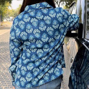 May include: A blue button-down shirt with a repeating white and blue geometric pattern. The long-sleeved shirt is made of a lightweight fabric and is paired with blue jeans. The shirt has a classic collar and buttoned cuffs.