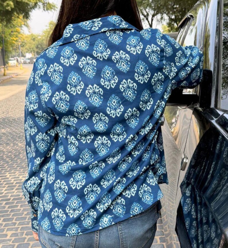 May include: A blue button-down shirt with a repeating white and blue geometric pattern. The long-sleeved shirt is made of a lightweight fabric and is paired with blue jeans. The shirt has a classic collar and buttoned cuffs.