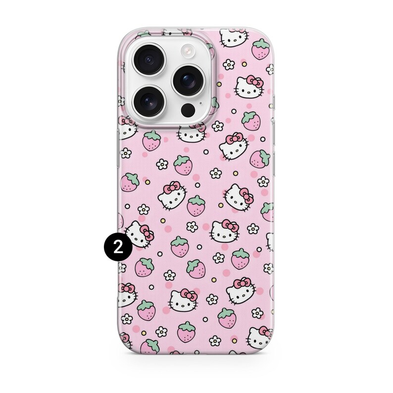 May include: A pink phone case featuring a repeating pattern of Hello Kitty faces, strawberries, and small white flowers. The case has a clear border and a camera cutout. The number "2" is printed in black on the lower left corner.