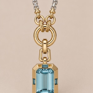 Peut inclure: Un collier pendentif en or avec une grande pierre précieuse rectangulaire bleu clair taille émeraude dans un cadre doré orné de petites pierres bleues, suspendu à un connecteur en or texturé et une chaîne en argent et or.