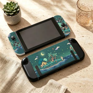 Pode incluir: Uma consola de jogos portátil com uma capa personalizada que apresenta uma cena noturna de uma ilha, incluindo uma lua crescente, palmeiras, uma casa pequena e um coelho a pescar junto à água. Os comandos a condizer são azul e turquesa.