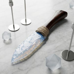 Puede incluir: Un cuchillo artesanal con un mango de madera oscura y una hoja translúcida y opalescente. La hoja está asegurada al mango con cuerda. El cuchillo se exhibe con formas geométricas decorativas y candelabros plateados.