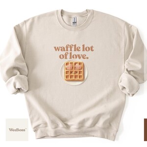 A cute, hand drawn waffle with heart toppings in soft colors - lifestyle image of a baby wearing a natural bodysuit in a scenic outdoor desert setting - exclusive WeeBoss print detail